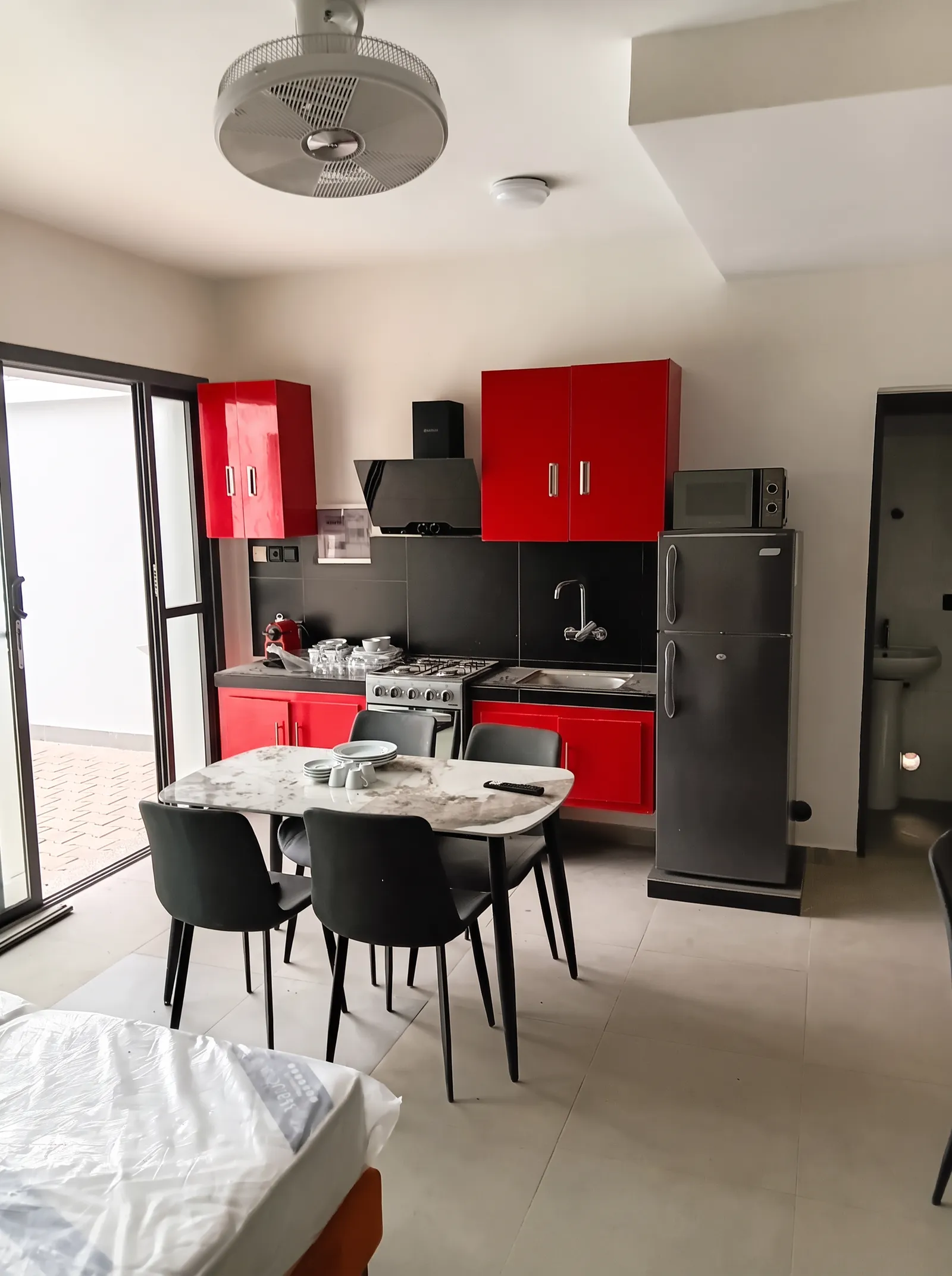 Espace de vie avec cuisine aux meubles rouges, table à manger et baie vitrée ouvrant sur la terrasse.
